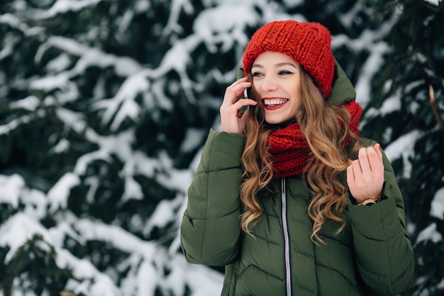 スマートフォンで話す赤い冬の帽子とスカーフの笑顔の女の子