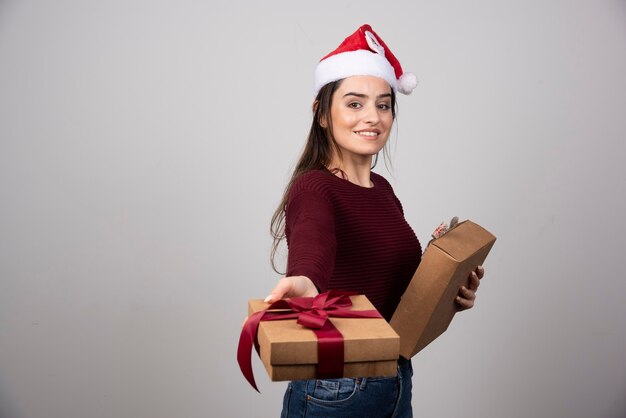Smiling girl in Santa hat offering gift box on gray background.