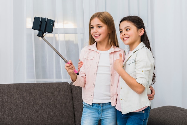 Free photo smiling girl showing thumb up sign taking self portrait with her friend