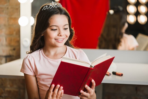 Smiling girl sitting at makeup room reading book