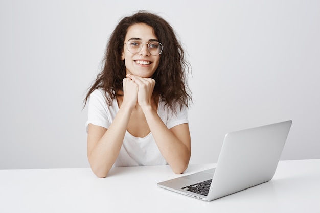 Ragazza sorridente che si siede vicino al computer portatile e che sembra incuriosita, pronta ad ascoltare