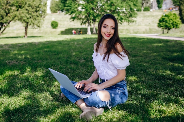 Smiling girl sitting in a park typing on her laptop