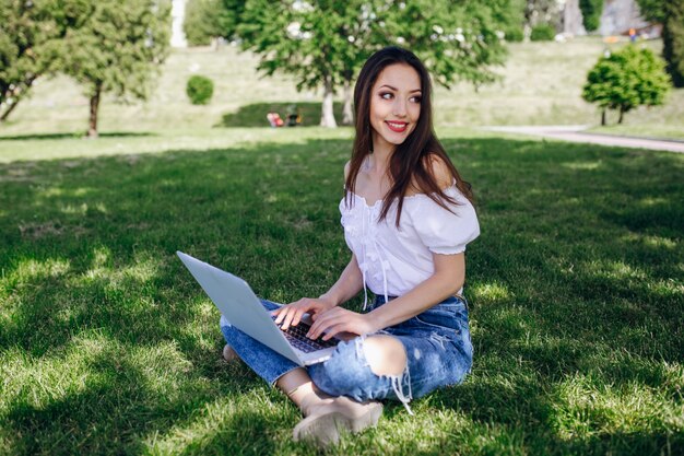 Smiling girl sitting in a park typing on her laptop