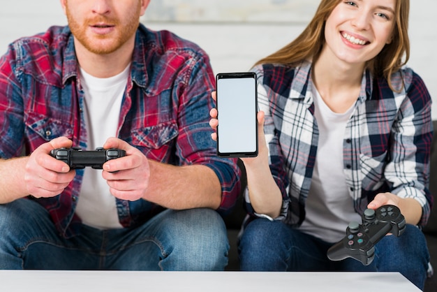 Free photo smiling girl sitting with her boyfriend playing video game showing mobile screen display