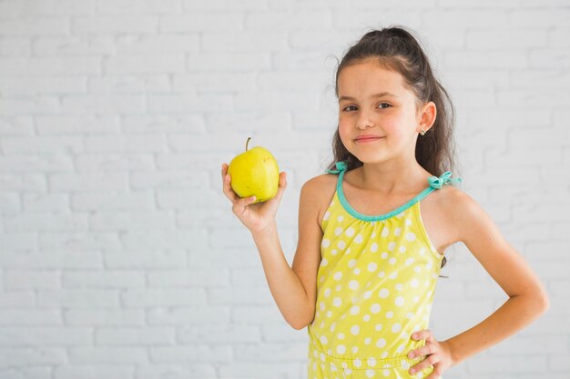 Smiling girl standing in front of white wall holding green apple