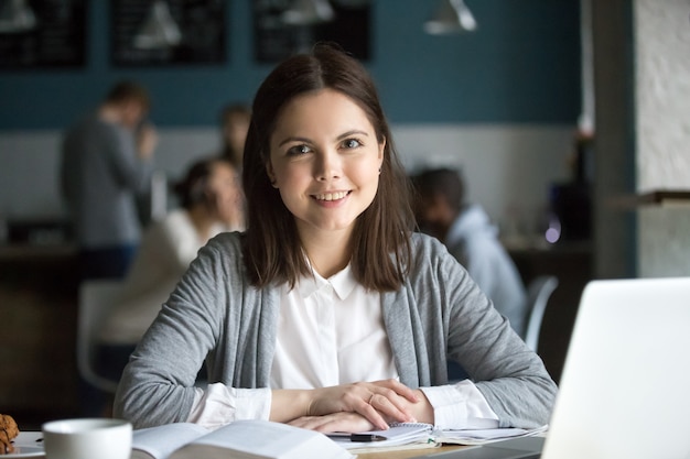 Foto gratuita studentessa sorridente che esamina macchina fotografica che si siede al tavolo del caffè