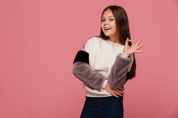 Smiling girl in sweater looking and showing ok gesture