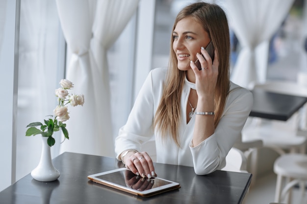 Smiling girl talking on the phone and touching the screen of a tablet