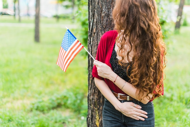 Foto gratuita ragazza sorridente con la bandiera americana davanti all'albero