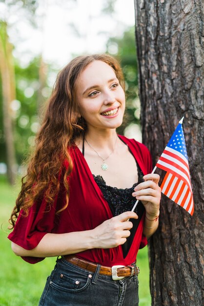 Smiling girl with american flag next to tree