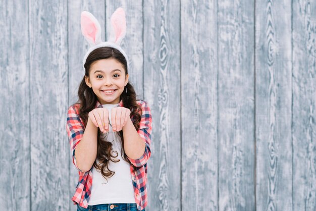 Smiling girl with bunny ears posing like rabbit against gray wooden desk