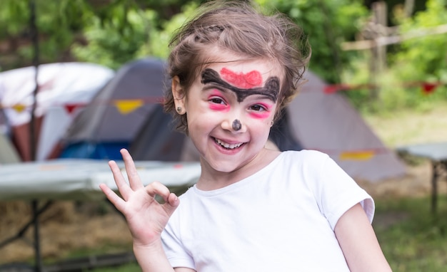 smiling girl with face art painting like tiger, little boy making face painting, halloween party, child with funny face painting