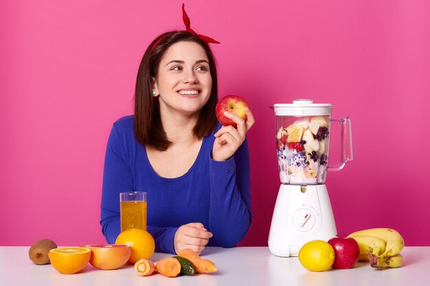 Smiling girl with fresh fruits on table isolated over pink