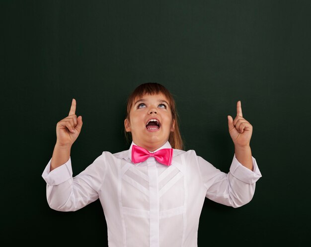 Smiling girl with pink bow tie pointing above her head