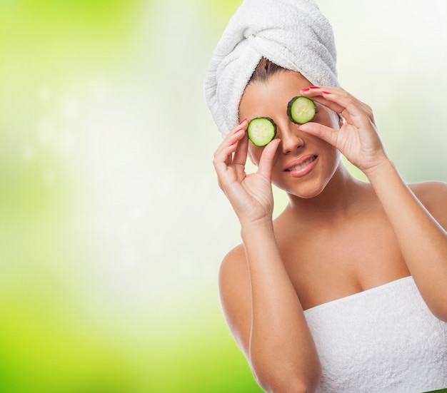 Smiling girl with towel on head and cucumbers on eyes