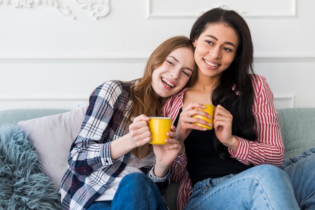 Smiling girls sitting nearby and holding yellow cups in hands