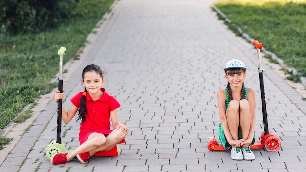 Free photo smiling girls sitting on their push scooter