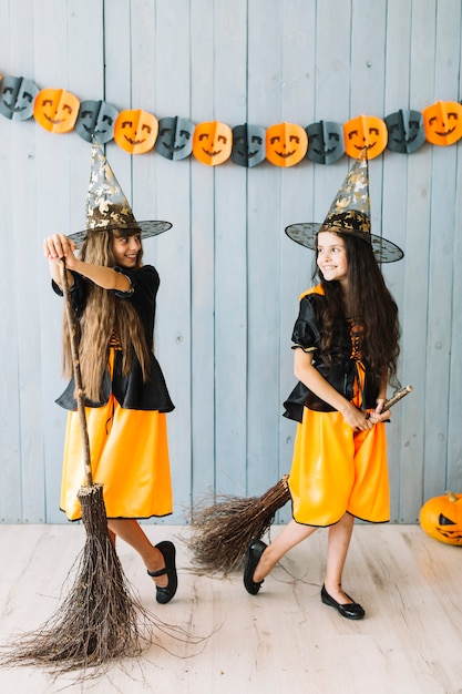 Smiling girls in witch suits holding broomsticks