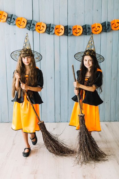Smiling girls in witch suits posing with broomsticks