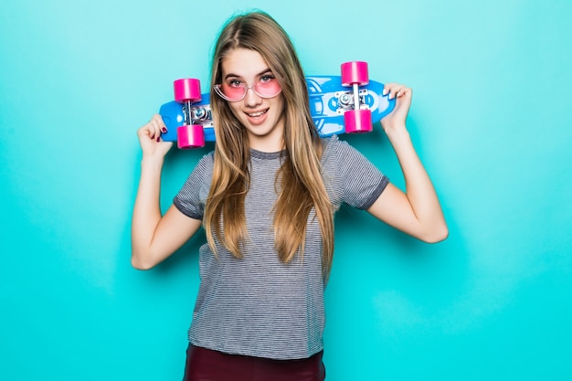 Smiling goldhaired Teenage skategirl stands with coloured skateboard isolated on green background