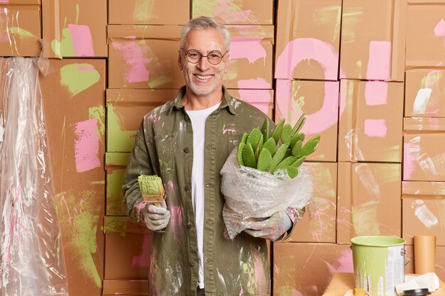 Smiling grey haired man in casual clothes renovates home paints walls in new apartment