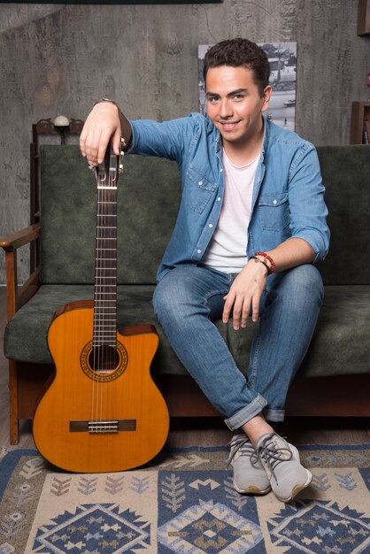 Smiling guitar player holding a beautiful guitar and sitting on sofa. High quality photo