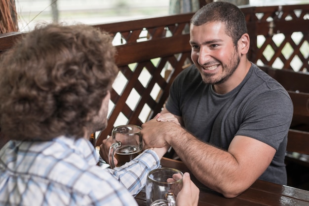 Free photo smiling guy arm wrestling with friend in bar