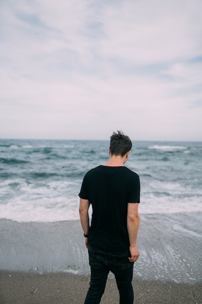 砂浜の海岸に立っている笑顔の黒いTシャツの男。