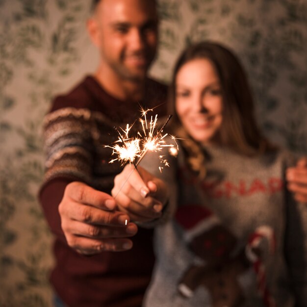 Smiling guy embracing cheerful lady with flaming Bengal lights 