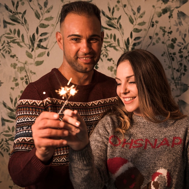 Smiling guy near cheerful lady with flaming Bengal lights 