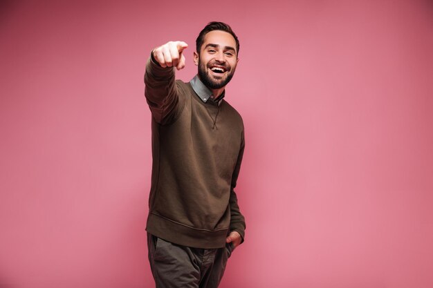 스웨터를 입은 웃는 남자는 분홍색 배경의 카메라에 손가락을 보여줍니다