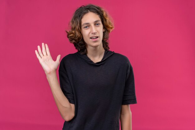 Улыбающийся парень с длинными волосами в черной футболке поздоровался на розовой стене