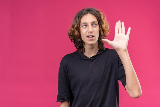 Smiling guy with long hair in black t-shirt showing five with his fingers on pink wall