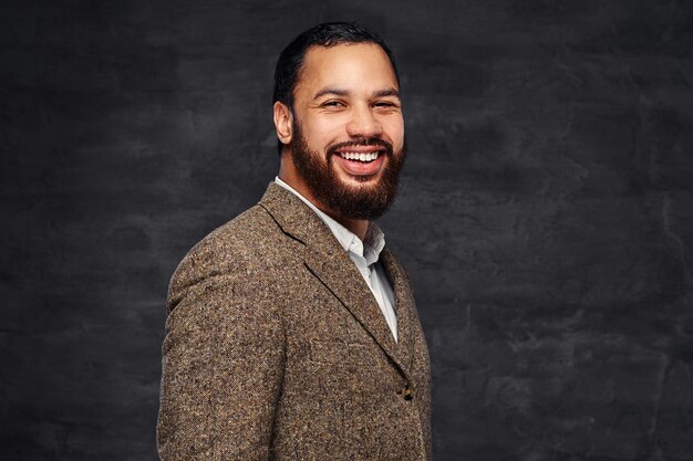 Smiling handsome bearded African-American businessman in a brown classic jacket. Isolated on a dark background.