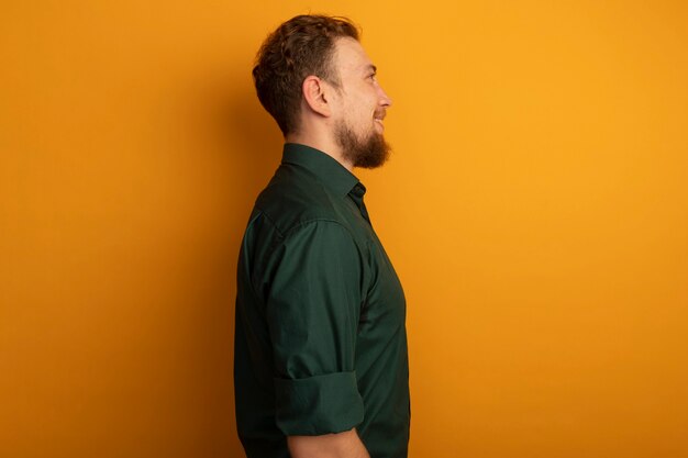 Smiling handsome blonde man stands sideways on orange