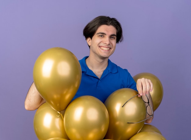 Smiling handsome caucasian man stands with helium balloons holding optical glasses 