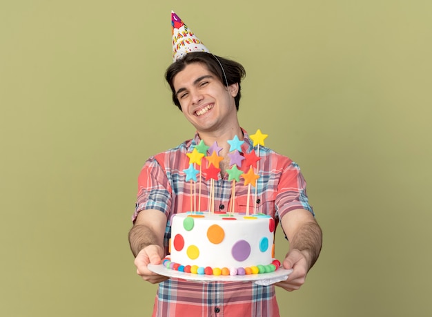 Smiling handsome caucasian man wearing birthday cap holds birthday cake 