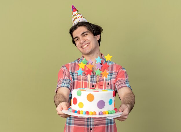 Улыбающийся красивый кавказский мужчина в кепке на день рождения держит праздничный торт