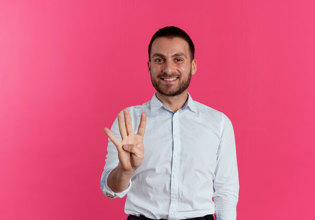 Smiling handsome man gestures four with hand isolated on pink wall