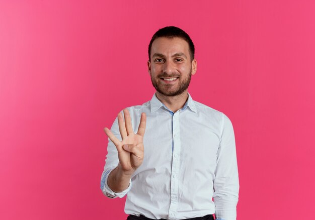 Улыбающийся красавец жестами четырех с рукой, изолированной на розовой стене