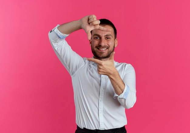 Smiling handsome man gestures frame hand sign isolated on pink wall