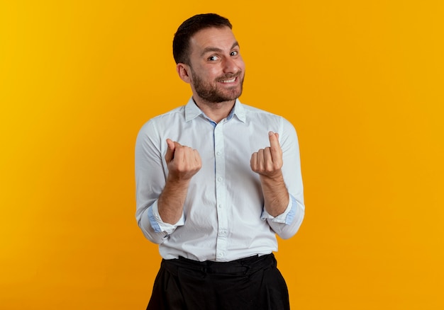 Smiling handsome man gestures money hand sign isolated on orange wall