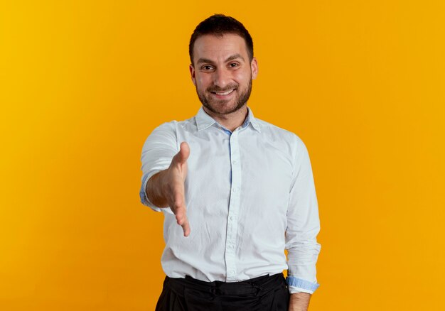 Smiling handsome man holds hand out isolated on orange wall