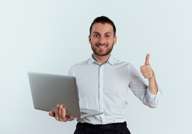 Smiling handsome man holds laptop thumbs up isolated on white wall