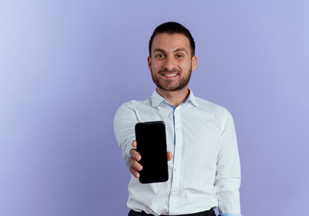 Smiling handsome man holds out phone isolated on purple wall