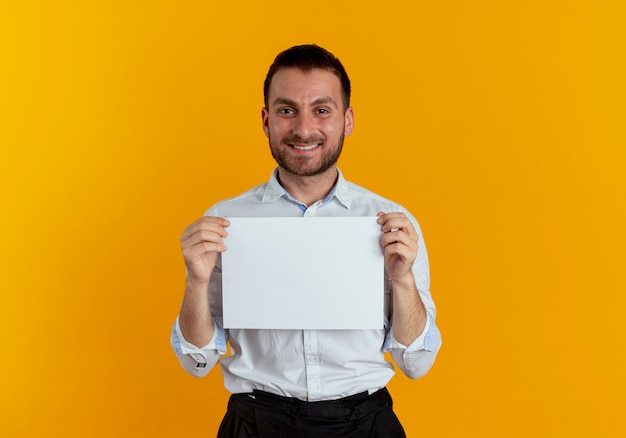L'uomo bello sorridente tiene il foglio di carta isolato sulla parete arancione