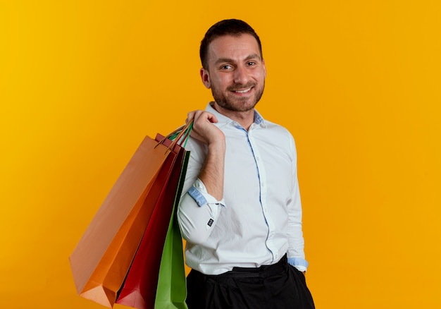 Smiling handsome man holds paper shopping bags on shoulder looking isolated on orange wall