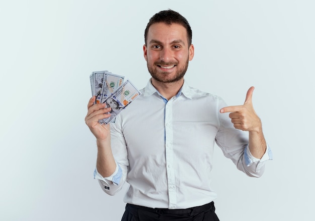 L'uomo bello sorridente tiene e indica soldi isolati sulla parete bianca