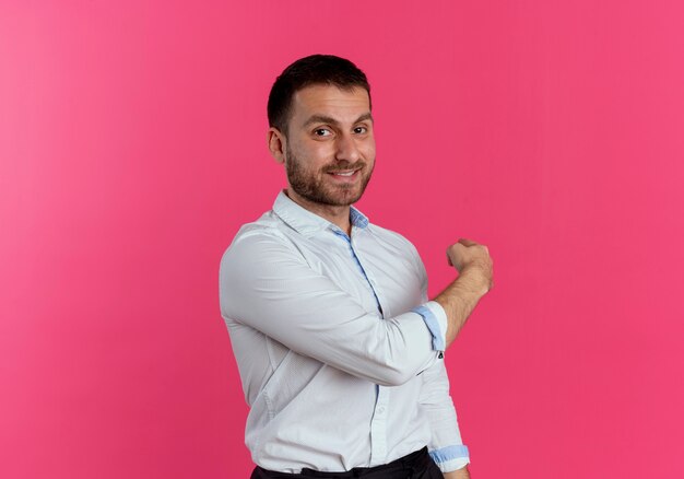 Smiling handsome man points back isolated on pink wall