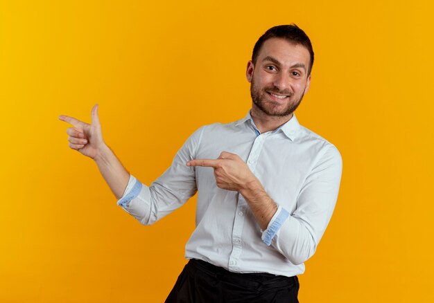 Smiling handsome man points at side with two hands isolated on orange wall